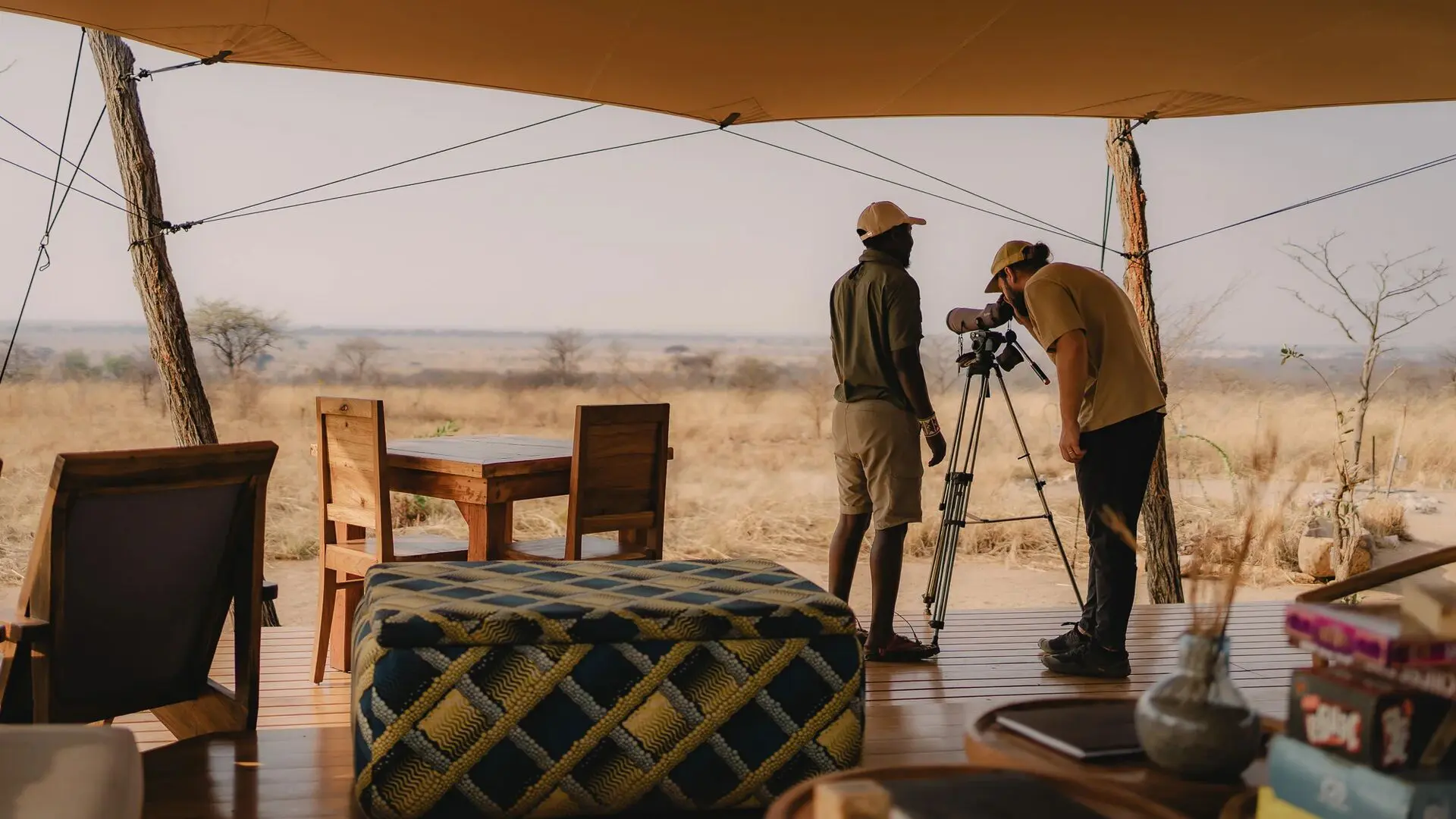 An Asilia guide and a guest using a telescope on a deck at Usangu Camp to observe the distant wildlife