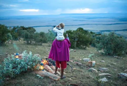 Kid on Masai's shoulders overlooking a view of the landscape near a wood fire