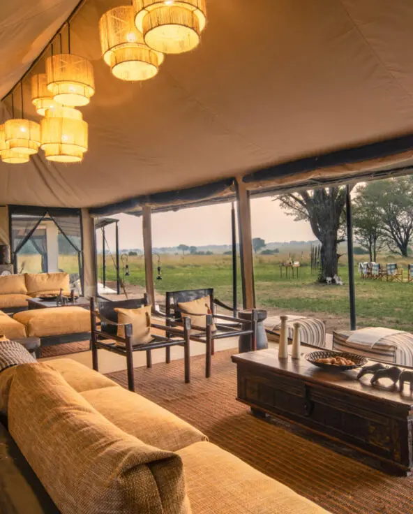 A gently lit and cosy lounge looks out from its tented structure onto the bush