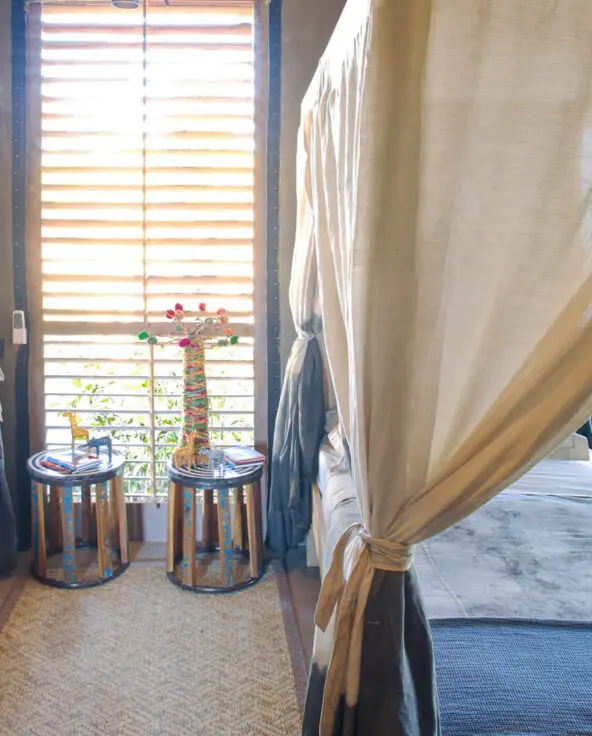 Jabali Private House, Ruaha National Park, twin beds with bedside tables with ornaments and mosquito nets hanging from the beds, rug between the beds