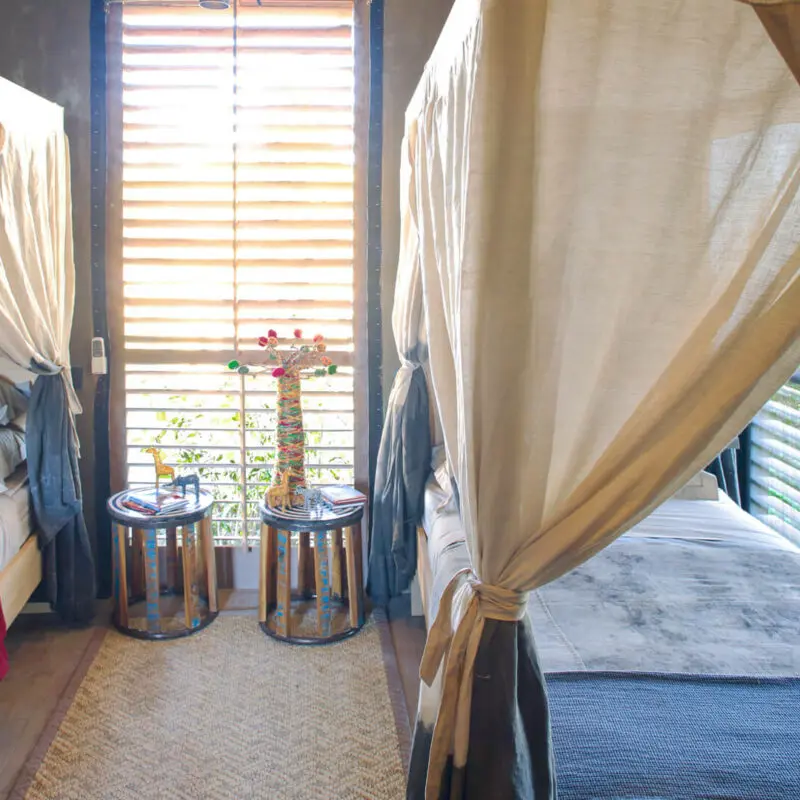 Jabali Private House, Ruaha National Park, twin beds with bedside tables with ornaments and mosquito nets hanging from the beds, rug between the beds