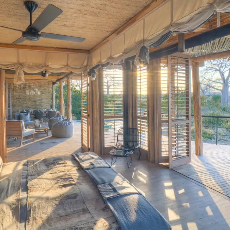 Jabali Private House, Ruaha National Park, double room interior with double bed with pillows and throw blanket, shutters open to the deck and main area, chair in the corner