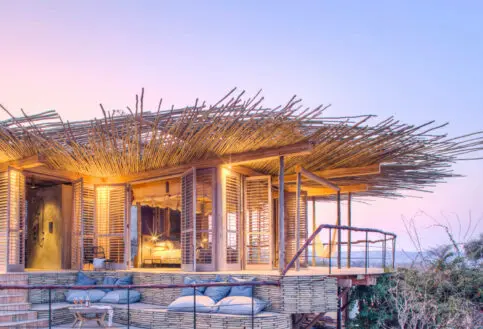 Jabali Ridge, Ruaha National Park, open shutters outside guest room with deck and seating area with pillows, drinks on the table, sunset in the background