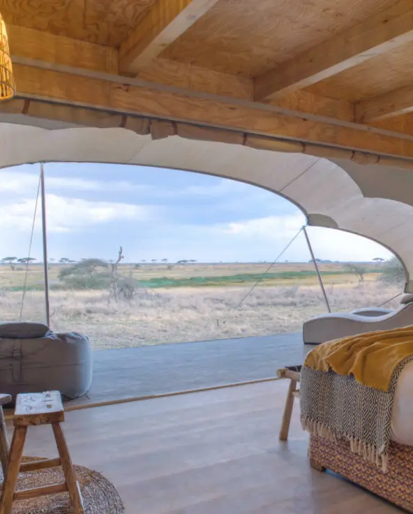 Namiri Plains, Serengeti National Park, guest tent interior, hanging lights, couches, bed made, curtains drawn and doors open