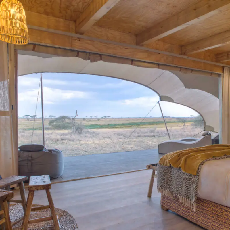 Namiri Plains, Serengeti National Park, guest tent interior, hanging lights, couches, bed made, curtains drawn and doors open