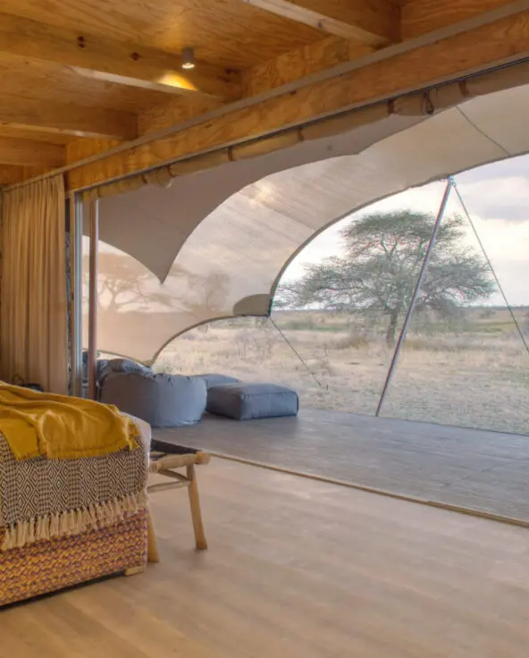 Namiri Plains, Serengeti National Park, guest tent interior, hanging lights, couches, bed made, curtains drawn and doors open