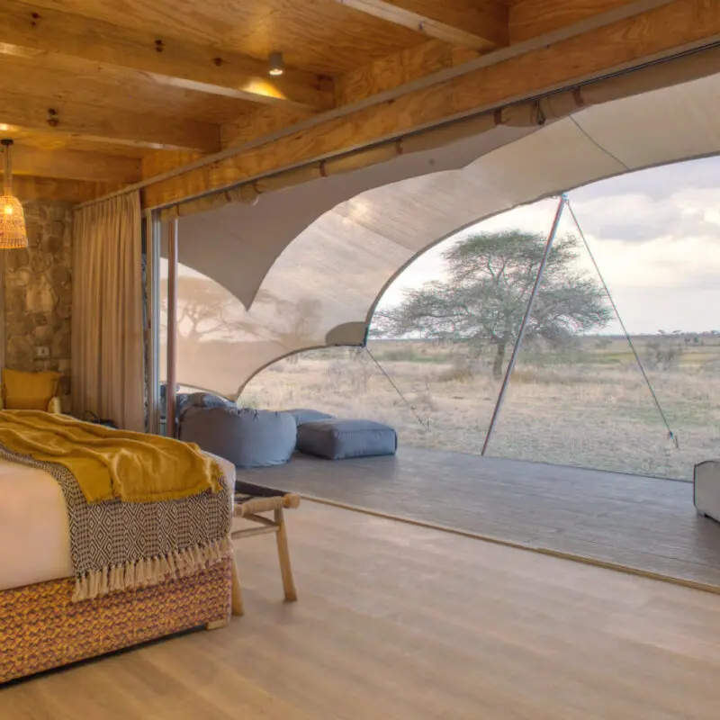 Namiri Plains, Serengeti National Park, guest tent interior, hanging lights, couches, bed made, curtains drawn and doors open