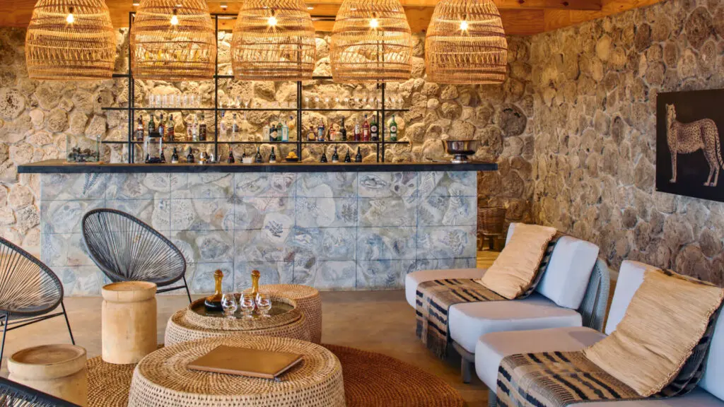 Namiri Plains, Serengeti National Park, bar at the main area, couches and wicker tables and chairs with shanga glass ornaments, hanging lights and cheetah infographic on the wall