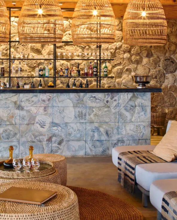 Namiri Plains, Serengeti National Park, bar at the main area, couches and wicker tables and chairs with shanga glass ornaments, hanging lights and cheetah infographic on the wall