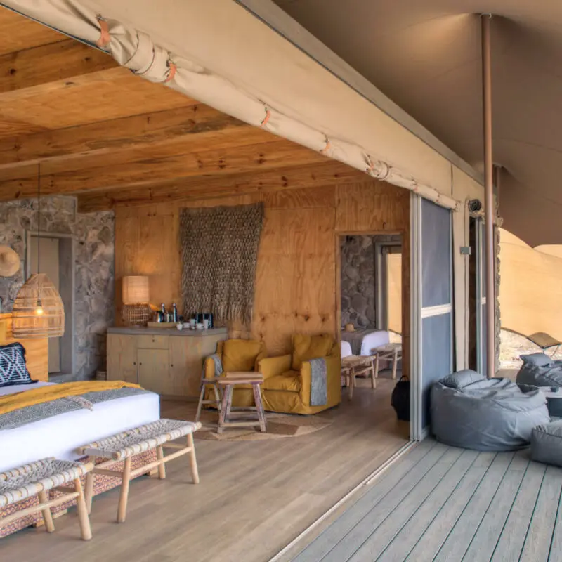 Namiri Plains, Serengeti National Park, view of the interior, double guest tent, bed with pillows and throw blanket, hanging lights, lamp on the side table with coffee station, bean bags on the deck, doors open