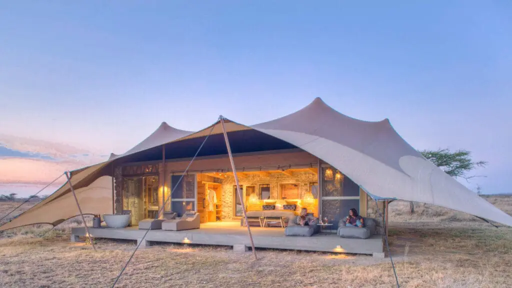 Namiri Plains, Serengeti National Park, guests having wine on the deck outside the tent, open doors, lights on and loungers on the deck with bath