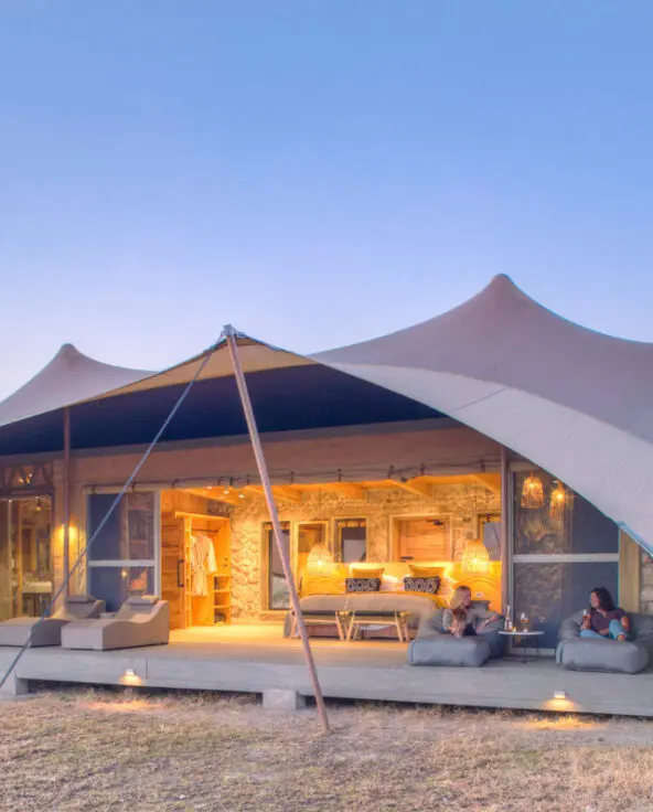 Namiri Plains, Serengeti National Park, guests having wine on the deck outside the tent, open doors, lights on and loungers on the deck with bath