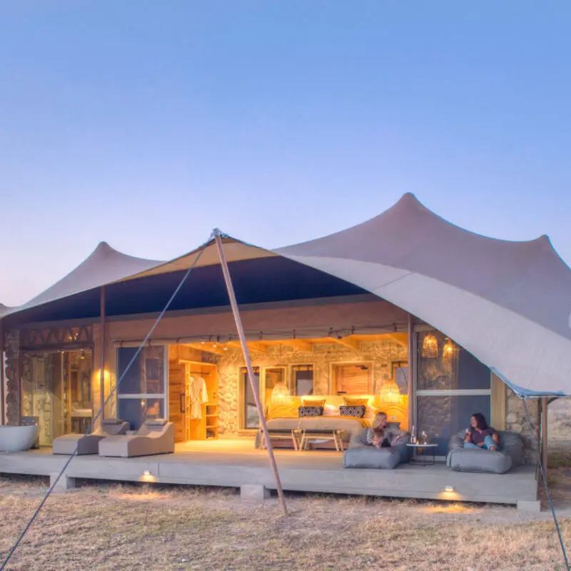 Namiri Plains, Serengeti National Park, guests having wine on the deck outside the tent, open doors, lights on and loungers on the deck with bath