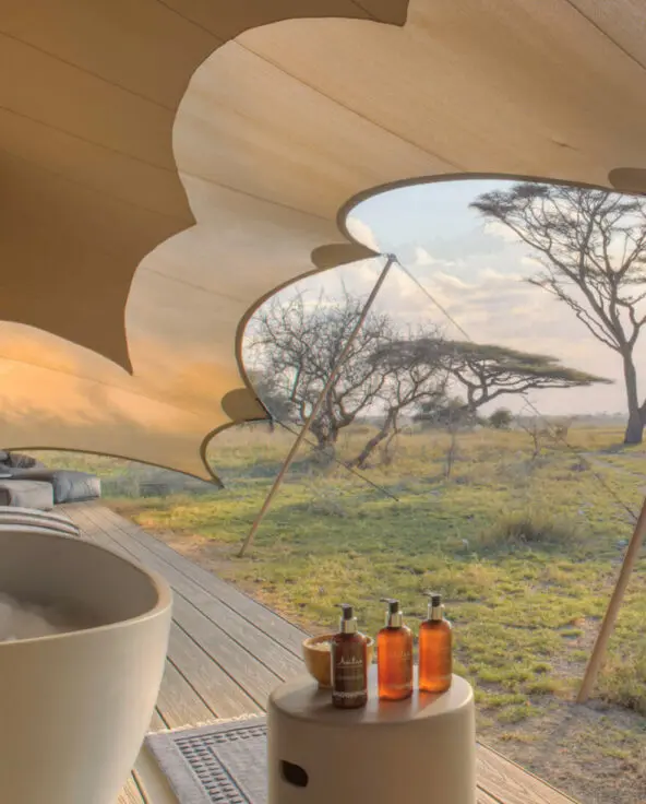Namiri Plains, Serengeti National Park, Bath on the deck with bubbles and wine glass and bottle, amenity bottles and bath salts, loungers and bean bags