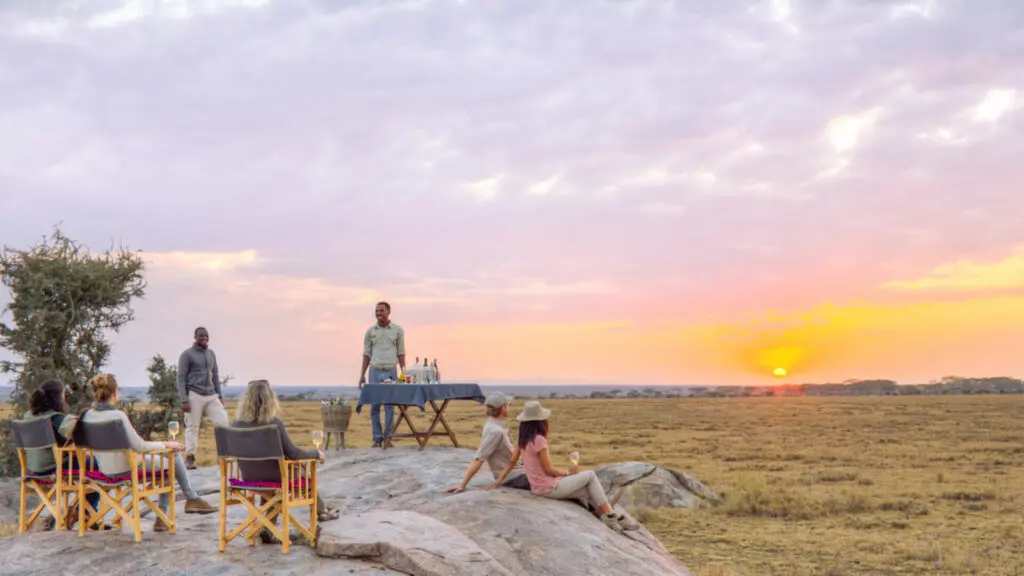 Namiri Plains, Serengeti National Park, guests drinking wine watching the sunset, chatting to guides, chairs and table with drinks