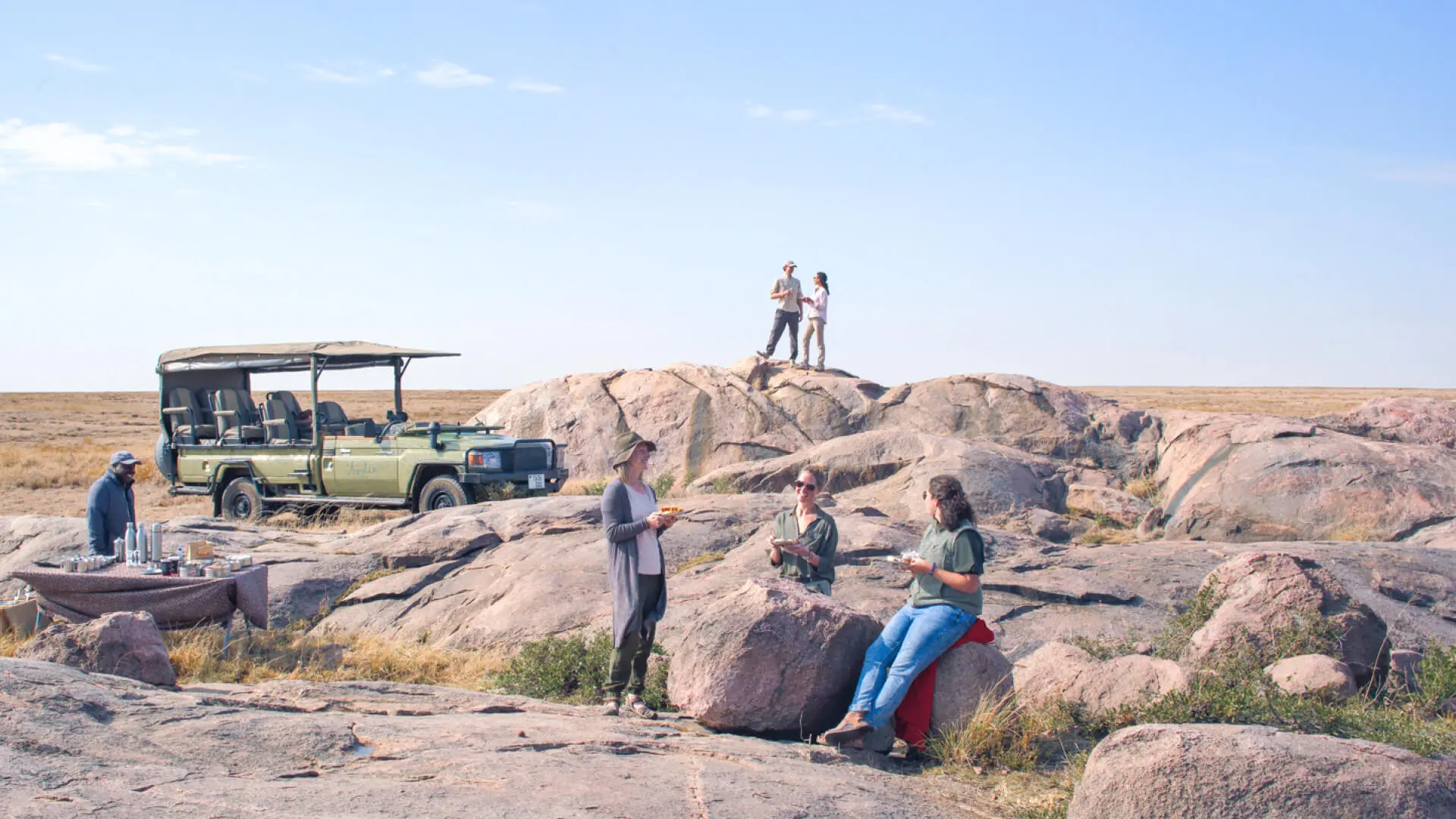Namiri Plains, Serengeti National Park, safari vehicle parked near some rocks, guests having lunch, table setup