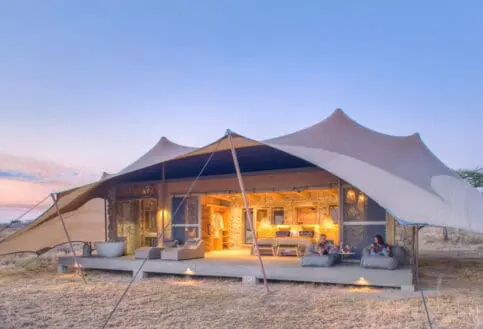 Namiri Plains, Serengeti National Park, guests having wine on the deck outside the tent, open doors, lights on and loungers on the deck with bath