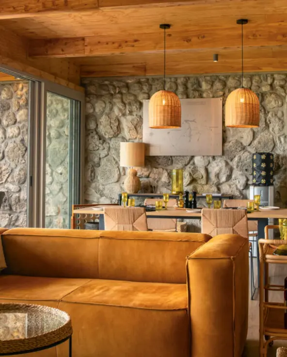 Namiri Plains Retreat, Serengeti National Park, lounge area interior, couch and table, tray of drinks and dining table setup for lunch, hanging lights and infographic on the wall