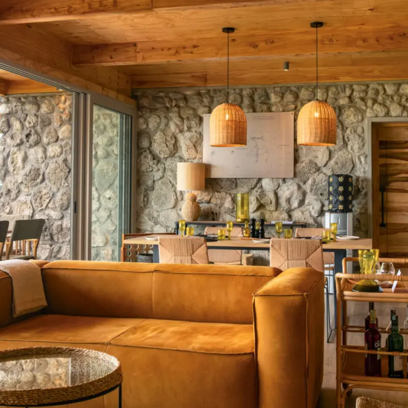 Namiri Plains Retreat, Serengeti National Park, lounge area interior, couch and table, tray of drinks and dining table setup for lunch, hanging lights and infographic on the wall