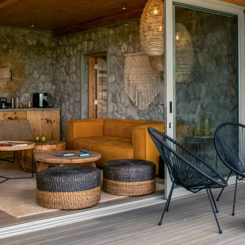 Asilia Namiri Plains Retreat, lounge area interior with couches, chairs, tables with books and scrabble, coffee station in the back, chairs and tables on the deck