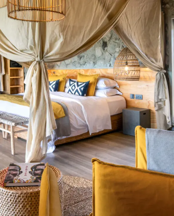 Namiri Plains Retreat, Serengeti National Park, guest room interior, double bed with pillows and blankets, couch and table with book, door to bathroom open