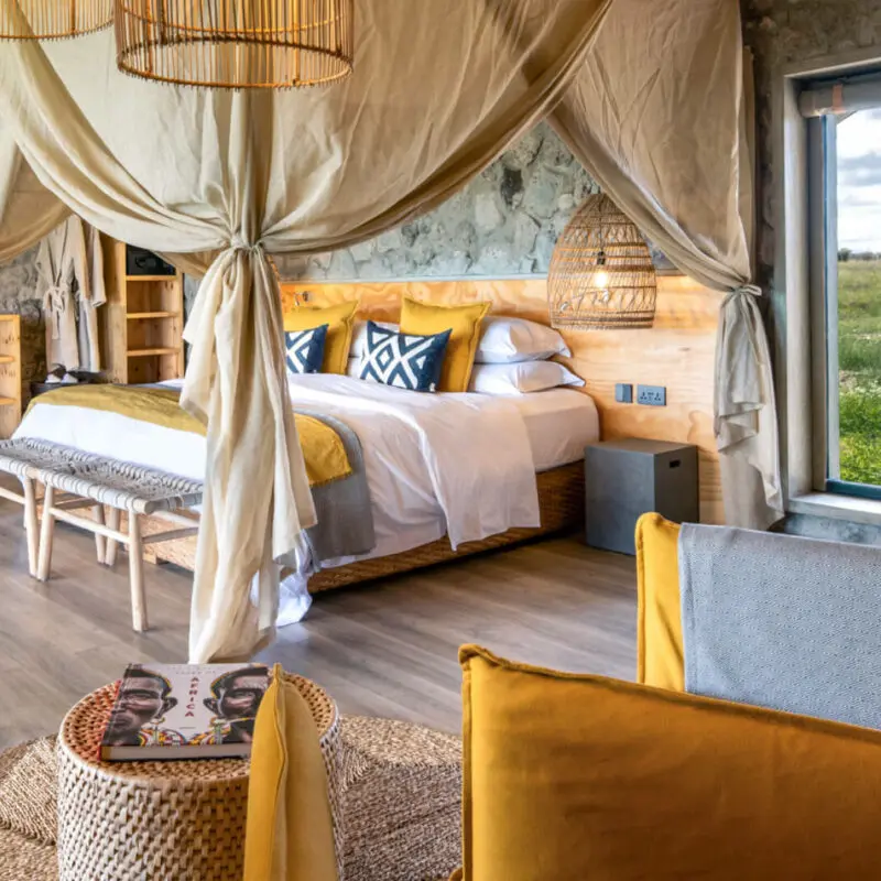 Namiri Plains Retreat, Serengeti National Park, guest room interior, double bed with pillows and blankets, couch and table with book, door to bathroom open