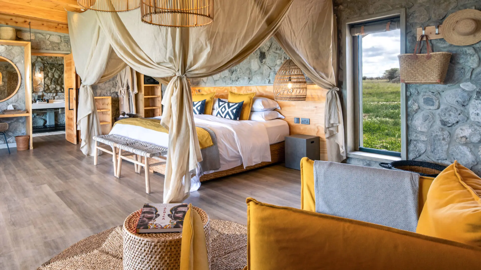 Namiri Plains Retreat, Serengeti National Park, guest room interior, double bed with pillows and blankets, couch and table with book, door to bathroom open