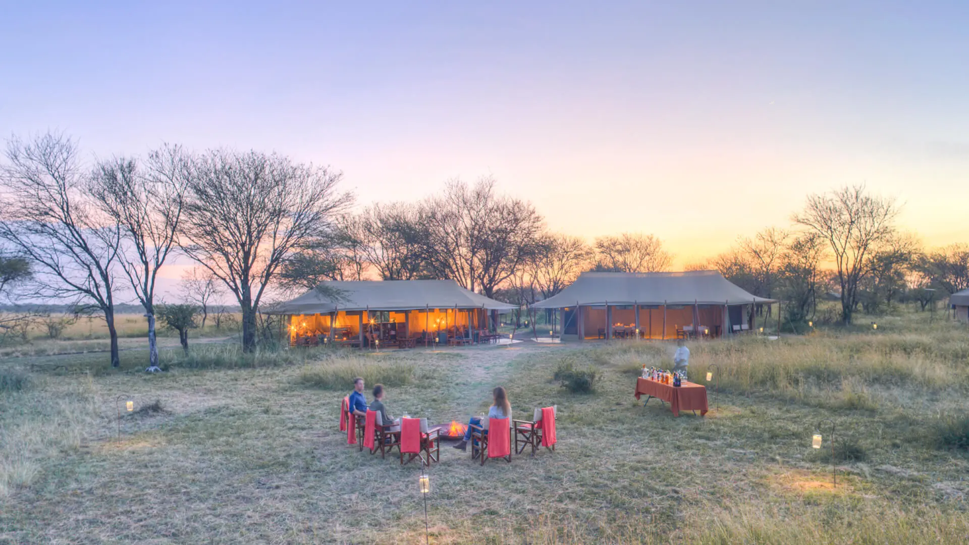 Guests enjoying sundowners around the campfire at camp, olakira migration camp, Serengeti National Park, Tanzania