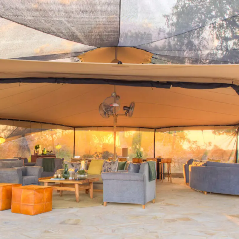 Roho ya Selous Camp, Nyerere National Park, sun shining through the main area at dusk, couches and ottomans