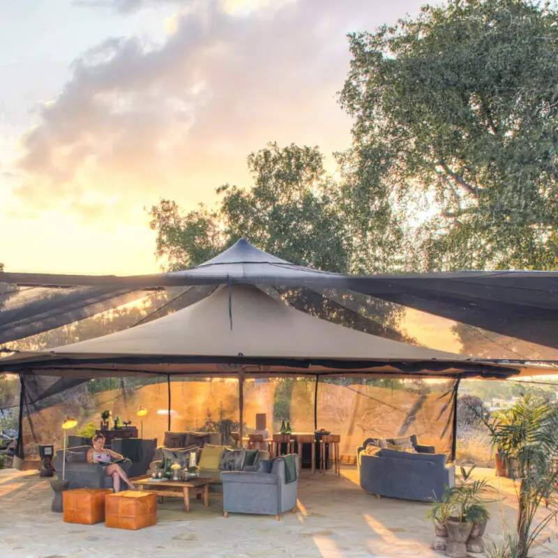 Roho ya Selous Camp, Nyerere National Park, guest sitting at the main area reading a book while the sun sets