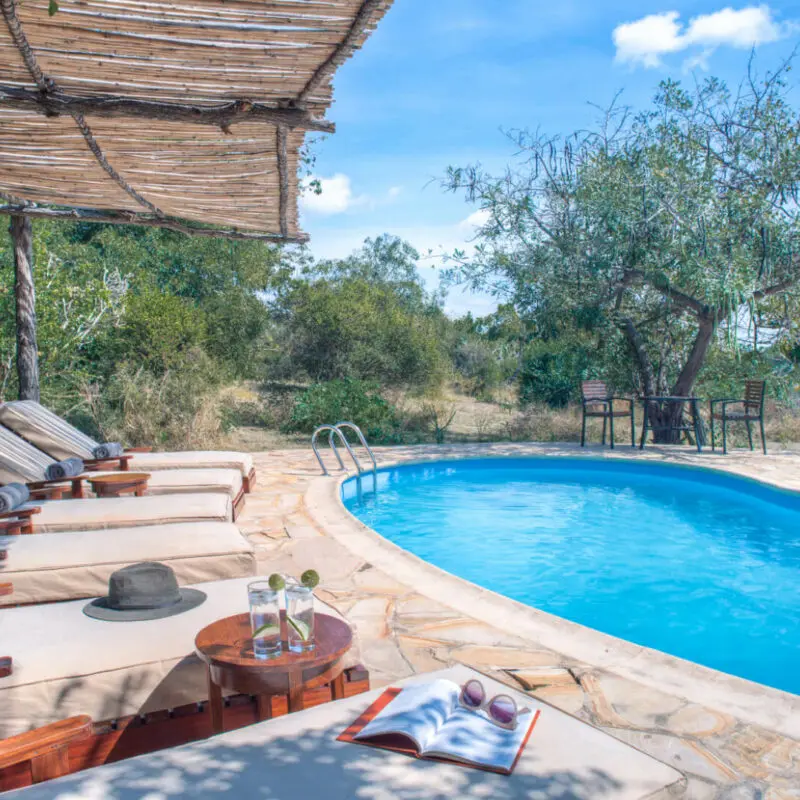 Roho ya Selous Camp, Nyerere National Park, loungers by the pool area, drinks on table, book and sunglasses and hat
