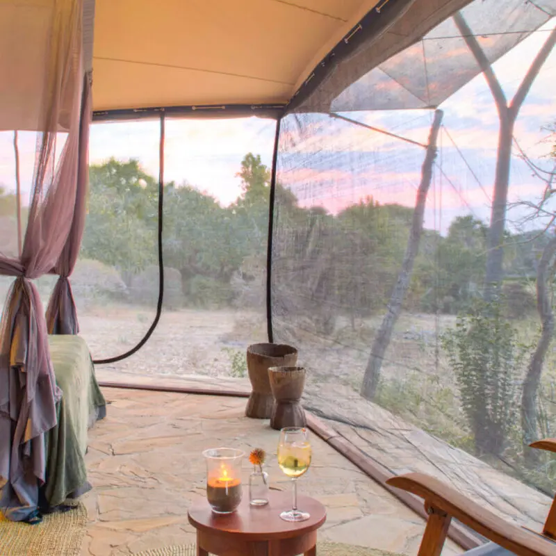 Roho ya Selous Camp, Nyerere National Park, double bed with netting around the room, table with glass of wine and chair in the foreground