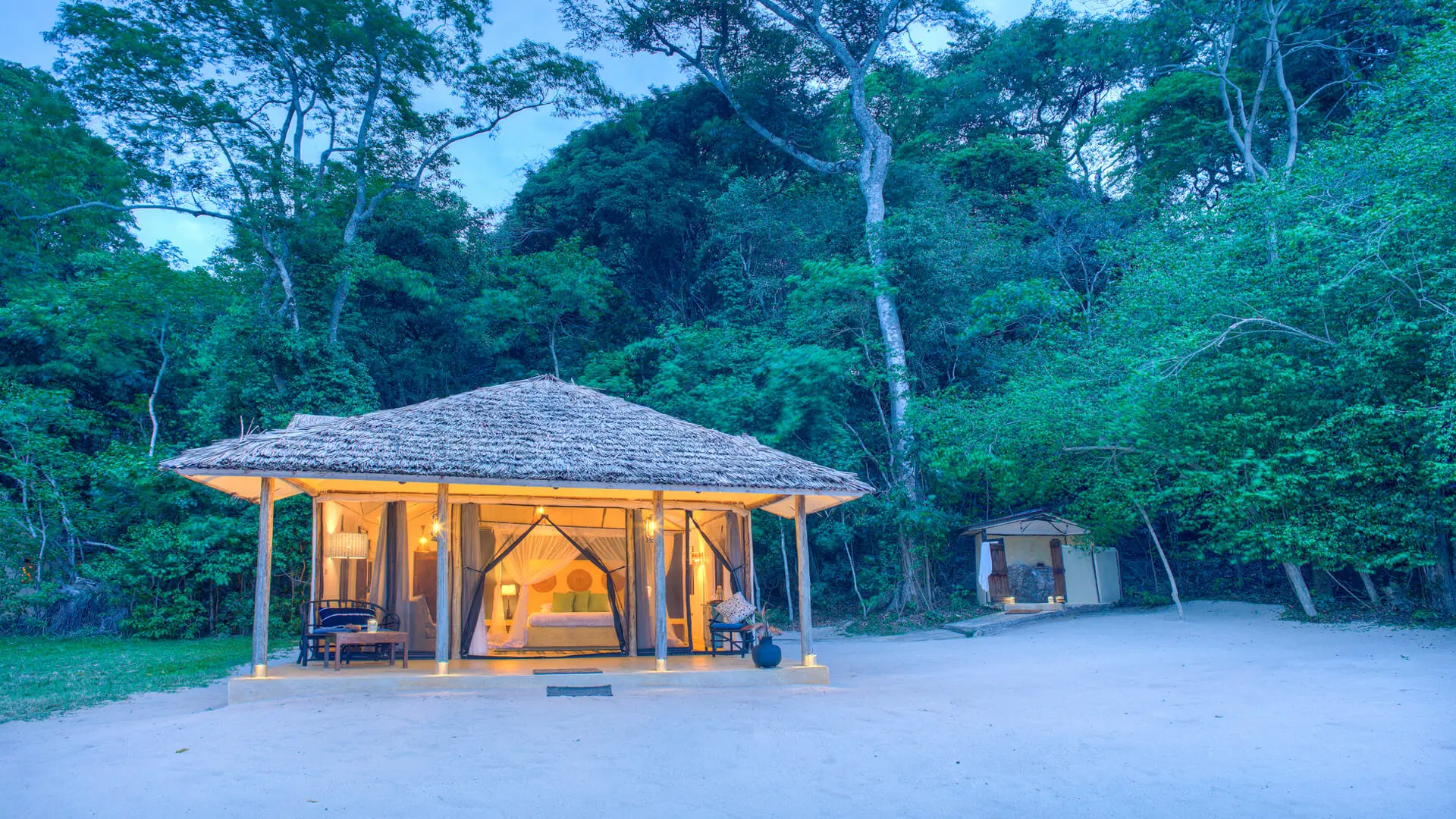 Rubondo Island Camp, Lake Victoria, exterior view of the chalet amongst the lush green trees lit up after dusk