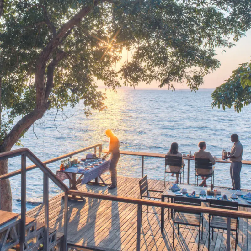 Rubondo Island Camp, guests being served coffee while they watch the sunrise, camp staff preparing breakfast setup