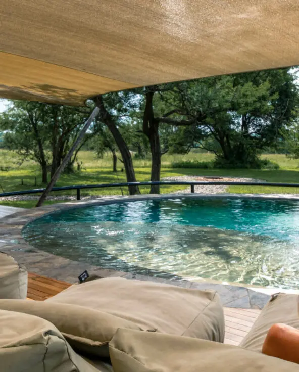 Sayari Retreat, Serengeti National Park, guest relaxing on a lounger by the pool surrounded by green trees