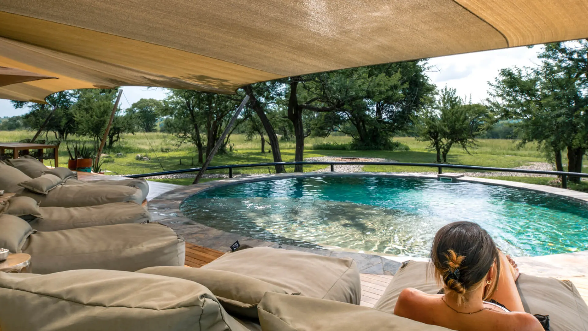 Sayari Retreat, Serengeti National Park, guest relaxing on a lounger by the pool surrounded by green trees