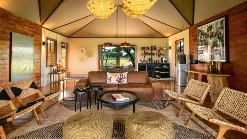 Sayari Retreat, Serengeti National Park, shared main area with couch, wicker chairs, tables books, shanga glass ornaments, bar and kitchen in the back