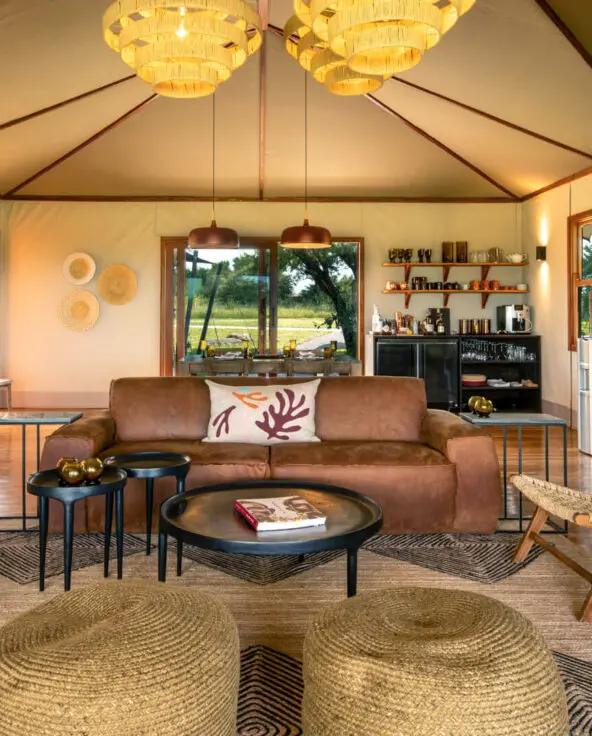Sayari Retreat, Serengeti National Park, shared main area with couch, wicker chairs, tables books, shanga glass ornaments, bar and kitchen in the back