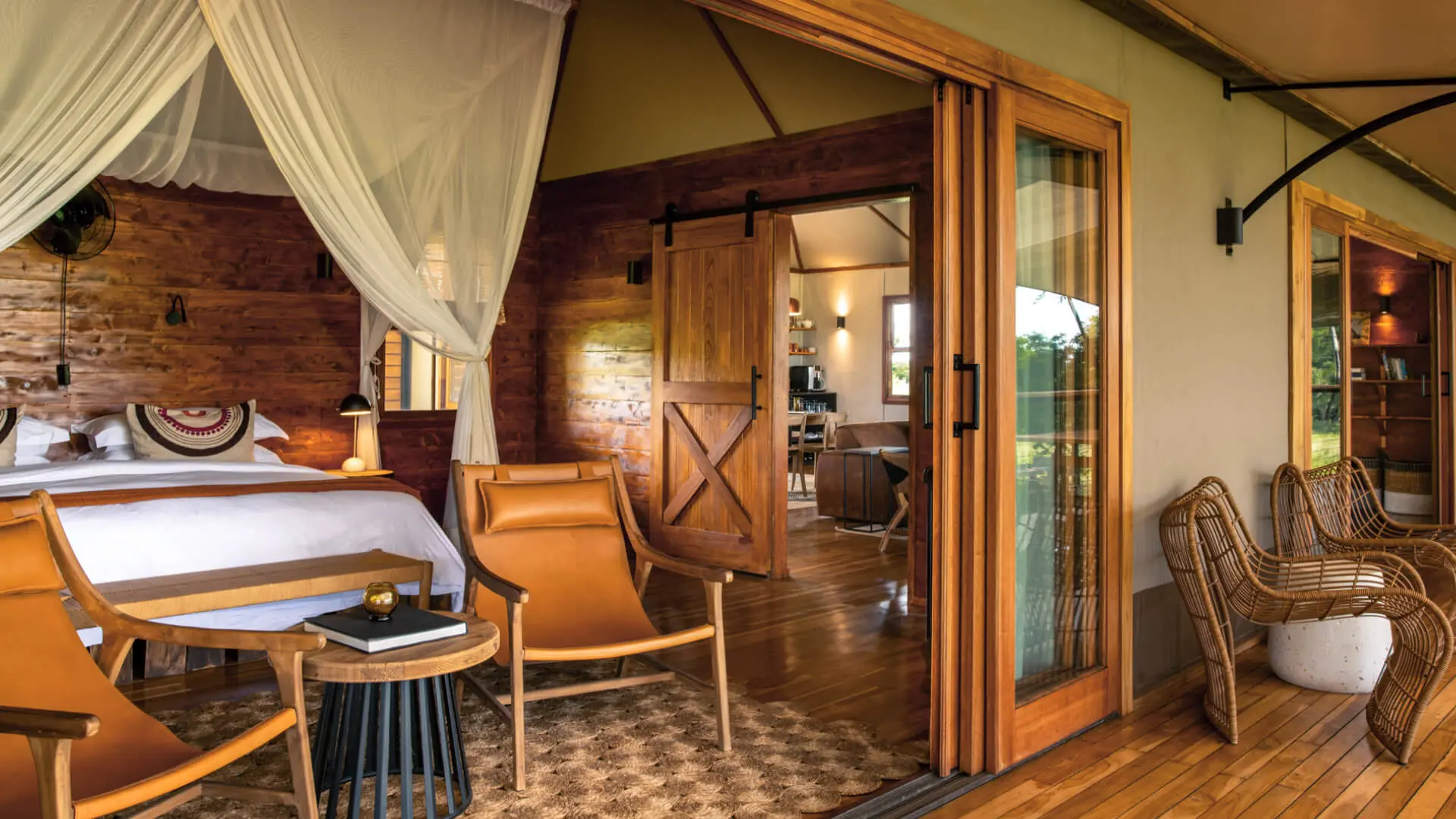 Sayari Retreat, Serengeti National Park, view of guest room interior from the deck, chairs and table with book, double bed with pillows and throw blanket, doors open