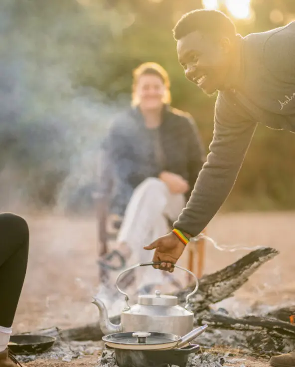 A waiter removes a kettle from the smoking fire to prepare meals for Asilia guests