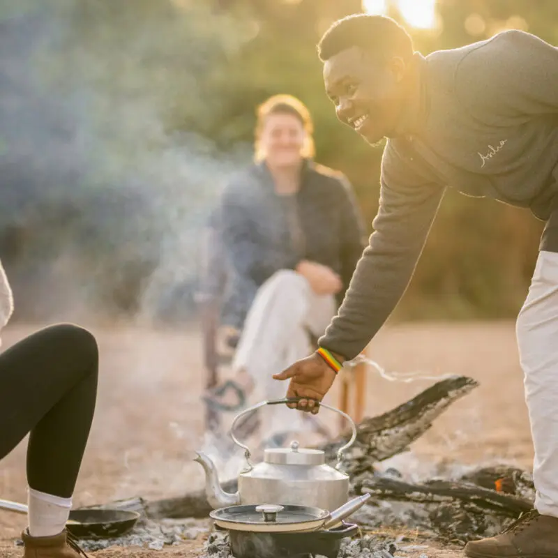A waiter removes a kettle from the smoking fire to prepare meals for Asilia guests