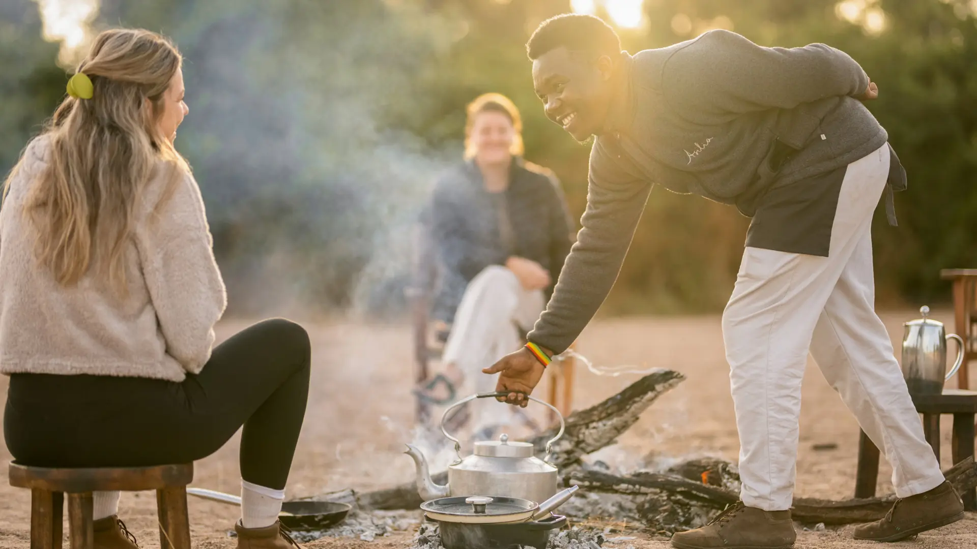 A waiter removes a kettle from the smoking fire to prepare meals for Asilia guests