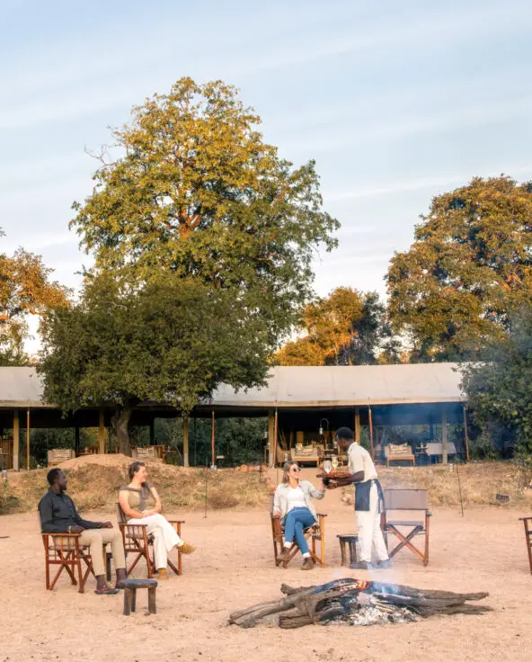 Guests enjoying sundowner drinks around the camp fire