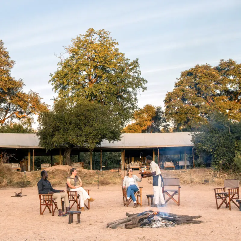 Guests enjoying sundowner drinks around the camp fire