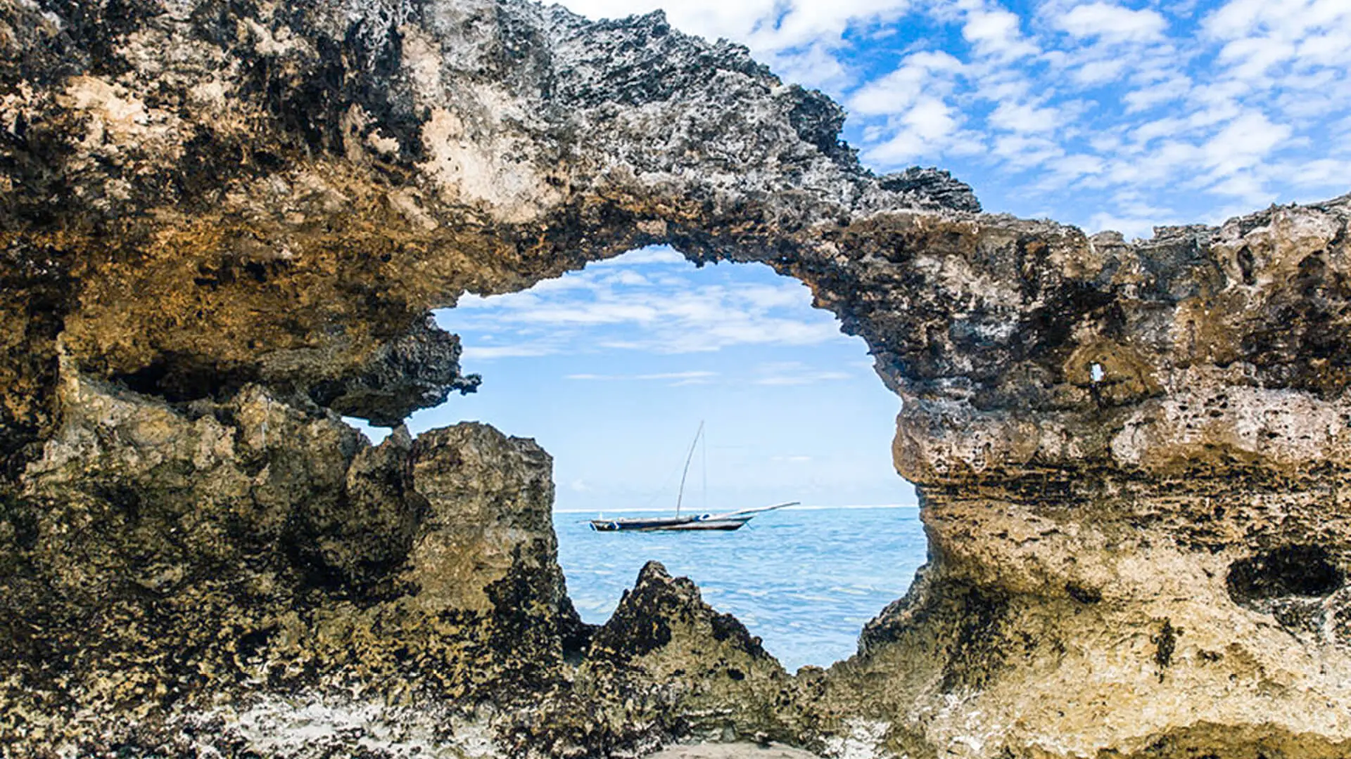 Through a hole in a rock formation a fishing boat can be seen in the water, Zanzibar.