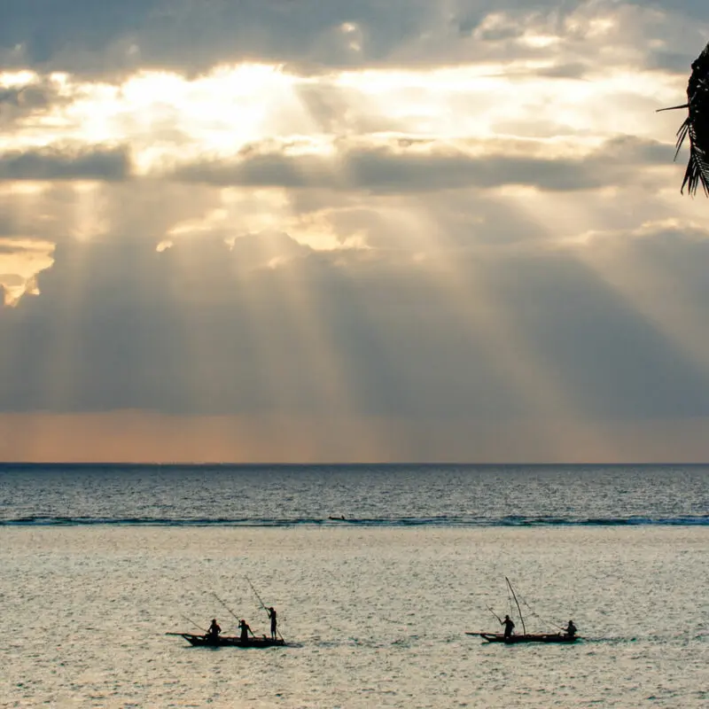 Two small fishing boats pass close to the shore in the early morning