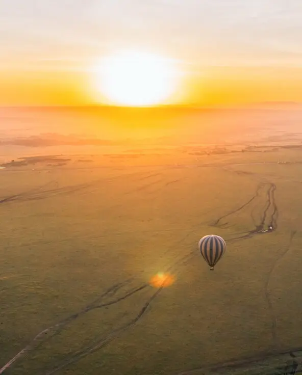 A hot air balloon glides over the plains at sunrise