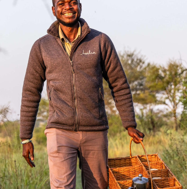 male asilia staff smiling at the camera, delivering morning coffe to guests, olakira camp, serengeti, tanzania, asilia africa