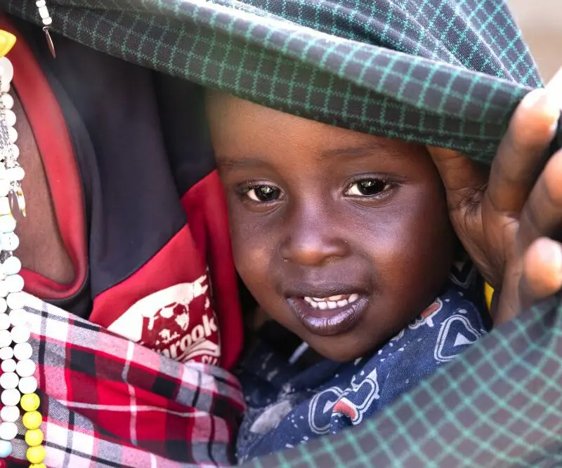 A young Maasai child peeks out from beneath a blanket