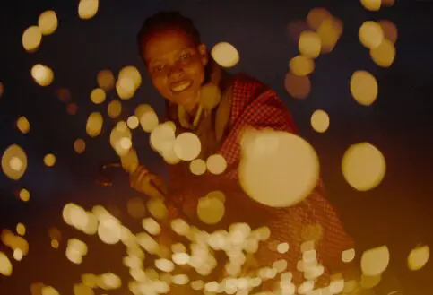 Evelyn stokes the fire, sending up a shower of glowing embers in the darkness.